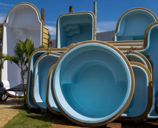 Stacked fiberglass pool shells in various shapes and sizes on display outdoors under a blue sky.