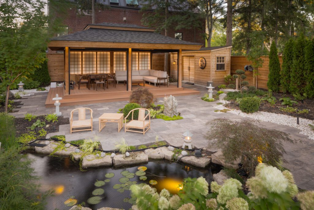 A natural looking pond with lilly pads, surrounded by grennery, is pictured amongst a garden area and Japanese-inspired lounging area and shed.