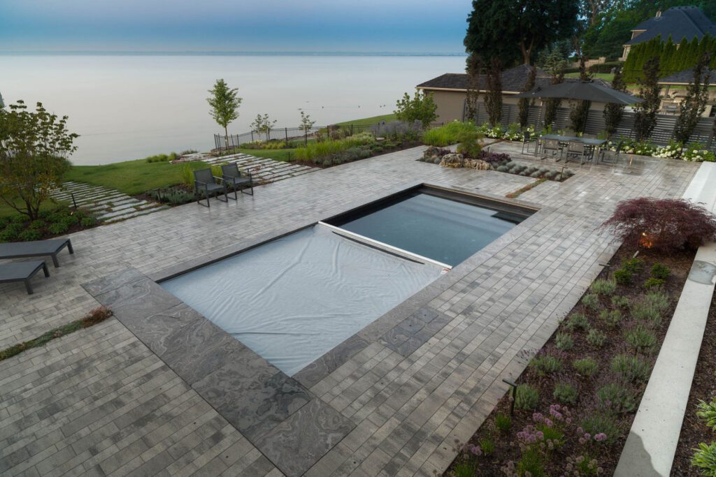 A backyard pool with a lake view in the background has its automatic pool cover covering half of the pool surface.