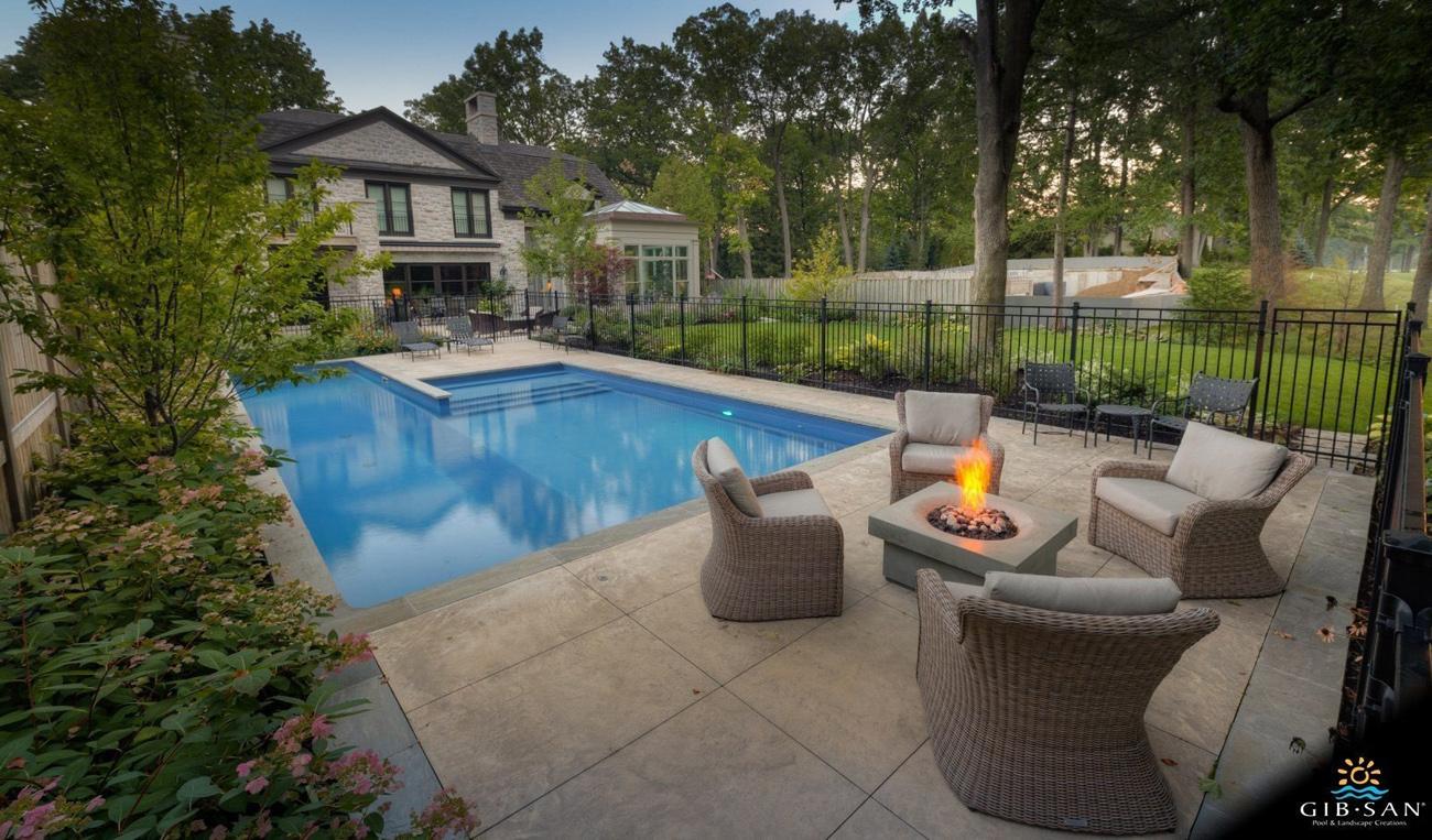View of a residential backyard of a home with a large pool area and lounging area with modern fire pit.