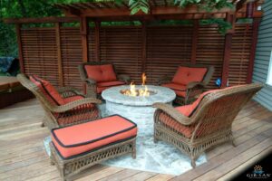 Four wicker chairs and an ottoman are shown around a raised stone fire pit.