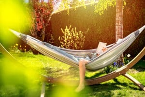 Young relaxed girl reading book in hammock in garden at home at bright sunset.