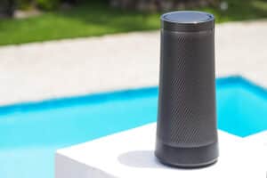 Modern portable music speaker with voice assistant near the swimming pool.