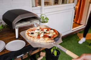 Freshly cooked and prepred pizza being taken out of a portable pizza oven in the garden outside.