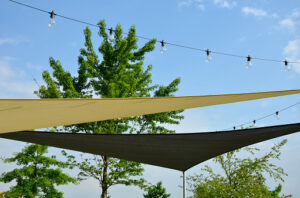 A light yellow canvas shade sail is stretched over an outdoor space, providing shade from the sun.