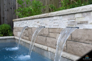 Close-up of a stone wall water feature with three spouting water falls going into a pool.