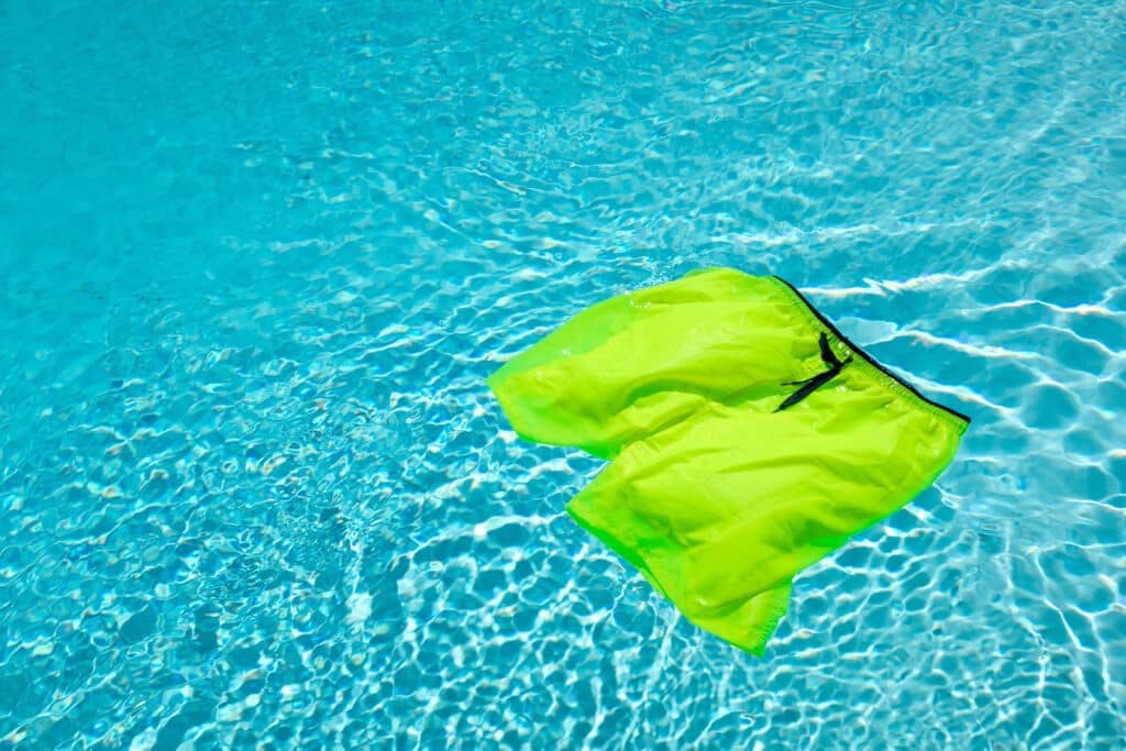 A pair of bight neon green swim trunks floats in a swimming pool