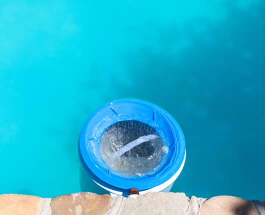 A plastic water filter near the stone wall of an outdoor swimming pool on a sunny day.