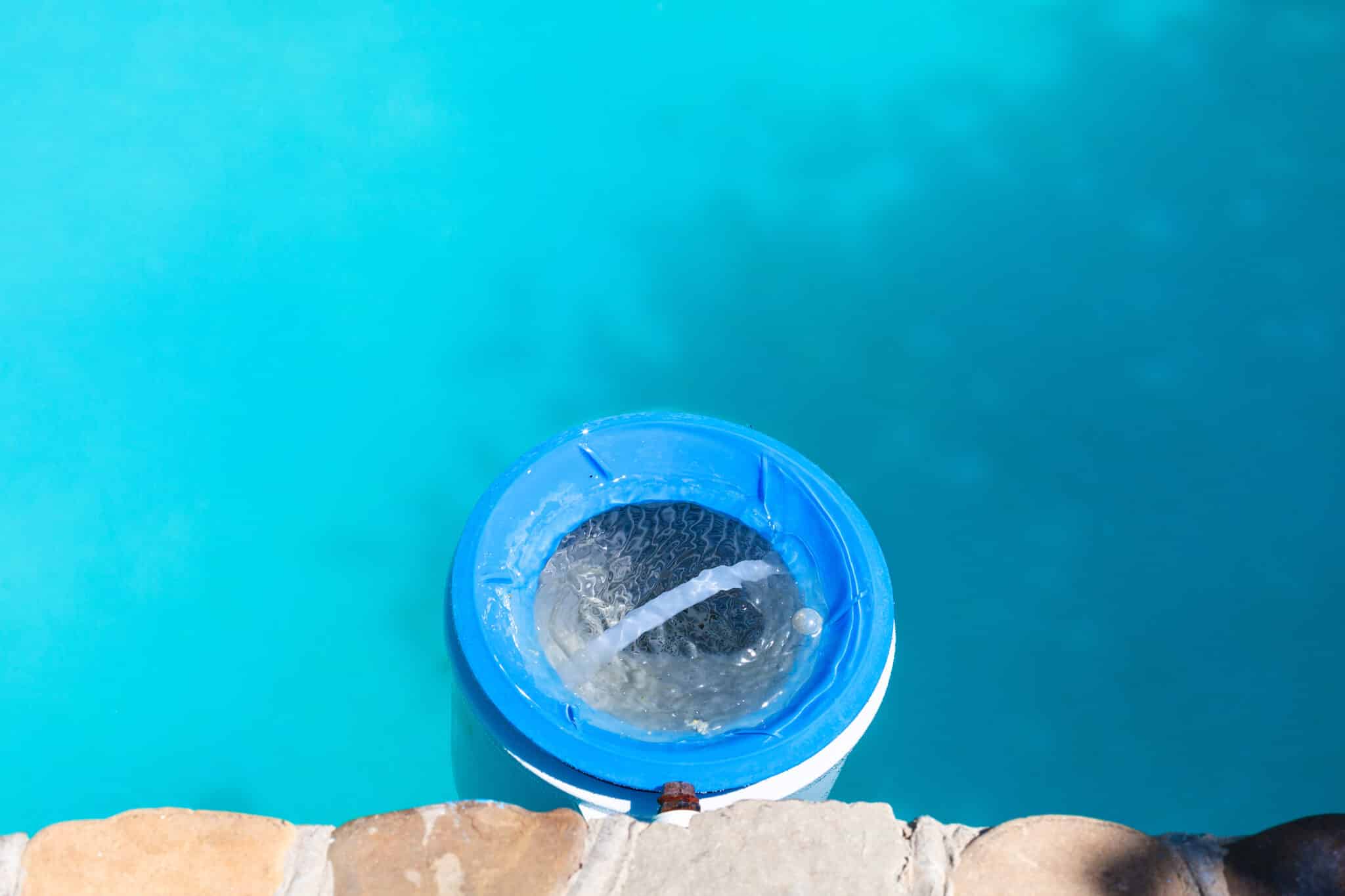 A plastic water filter near the stone wall of an outdoor swimming pool on a sunny day.