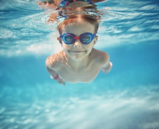 Portrait of smiling little boy enjoying an underwater swim in the pool towards the camera.