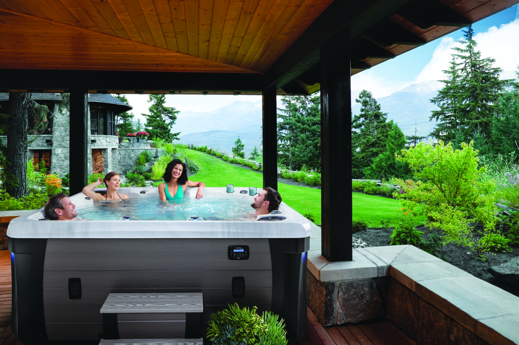 Two women and two men are sitting and laughing in a hot tub with the stunning view of trees and mountains in the background.