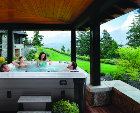 Two women and two men are sitting and laughing in a hot tub with the stunning view of trees and mountains in the background.