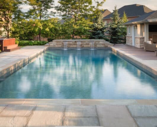 Head-on view of a vinyl swimming pool with three waterfall features at midday in a large suburban backyard.