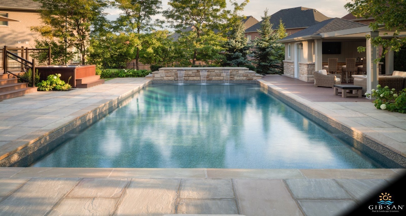 Head-on view of a vinyl swimming pool with three waterfall features at midday in a large suburban backyard.
