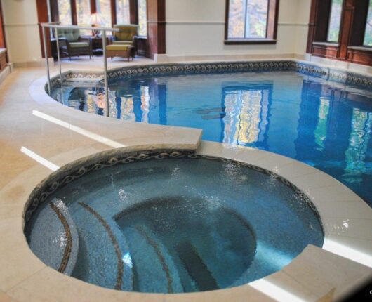 Indoor luxury pool with an adjacent circular spa featuring mosaic tilework, built-in seating, and curved steps.