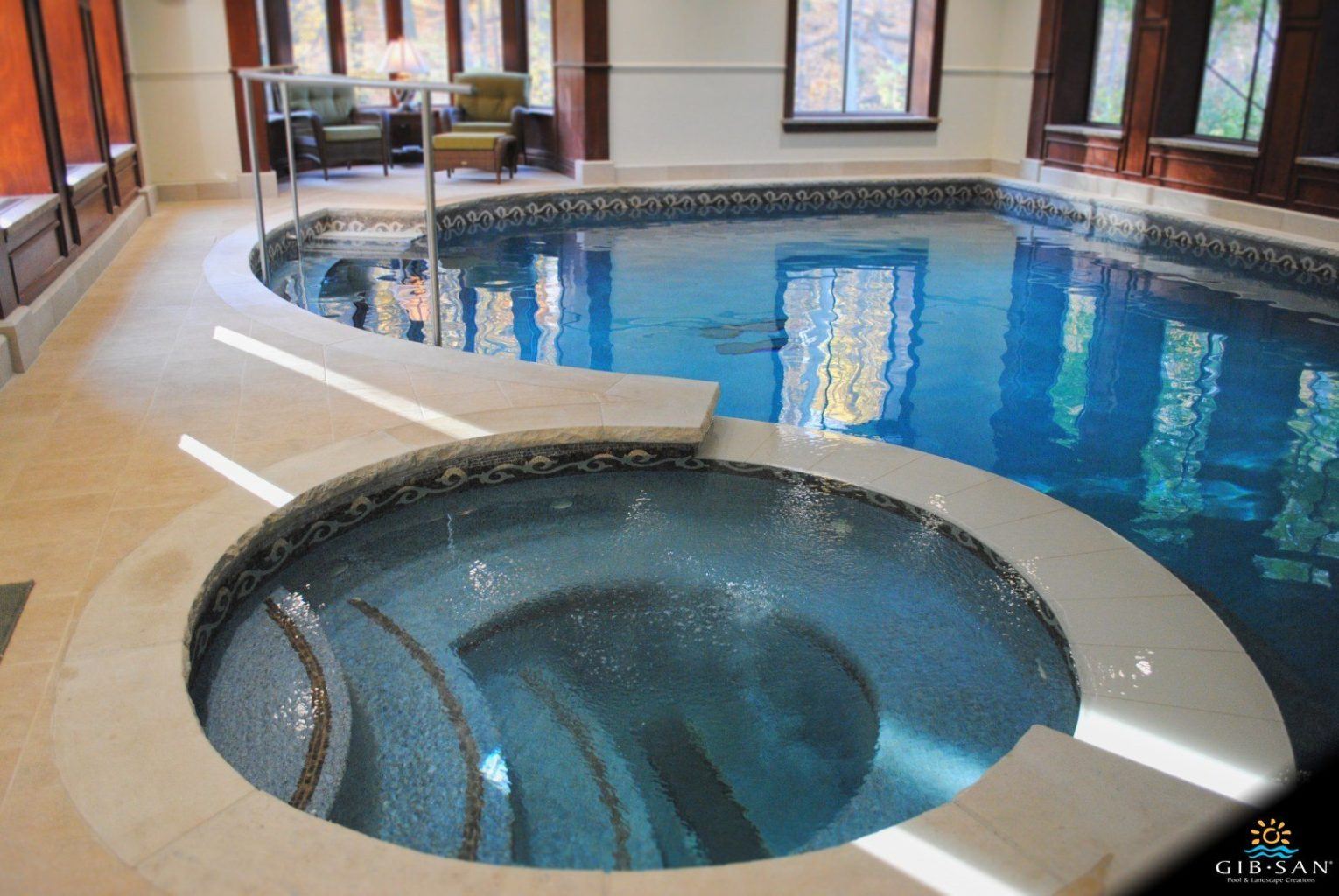 Indoor luxury pool with an adjacent circular spa featuring mosaic tilework, built-in seating, and curved steps.