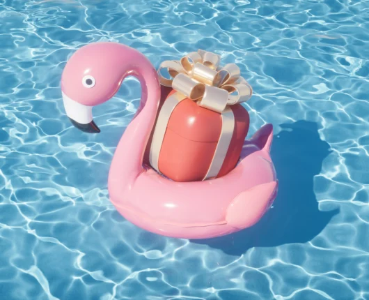 Pool and spa supplies gift concept with wrapped present on pink flamingo float in swimming pool.