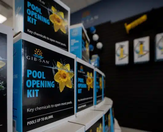 Row of Gib-San Pool Opening Kit boxes displayed on shelves in a pool supply store, with additional products and signage blurred in the background.