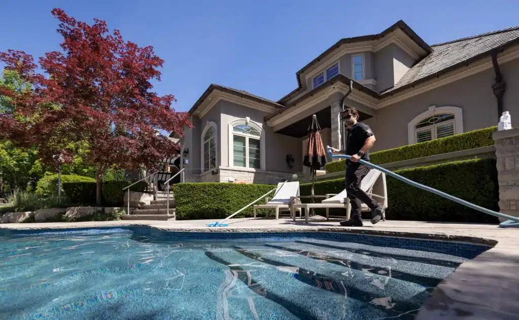Pool technician vacuuming and cleaning backyard swimming pool during professional pool opening service at residential home in Ontario.