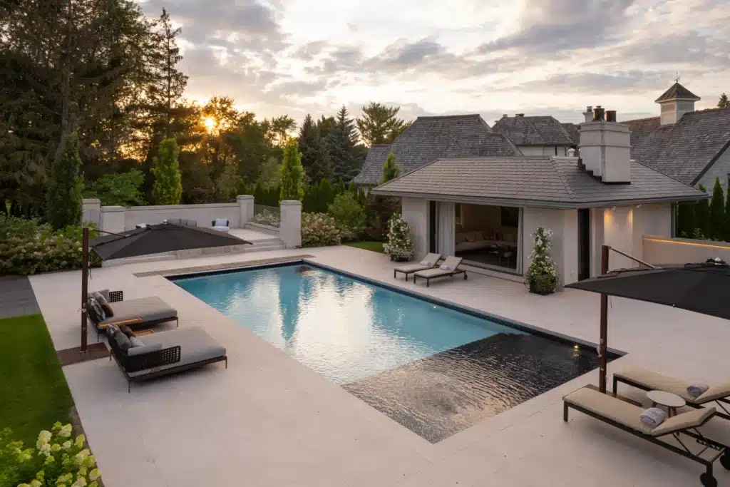 Luxury backyard swimming pool with modern pool house, lounge chairs, and landscaped patio at sunset in Ontario home.