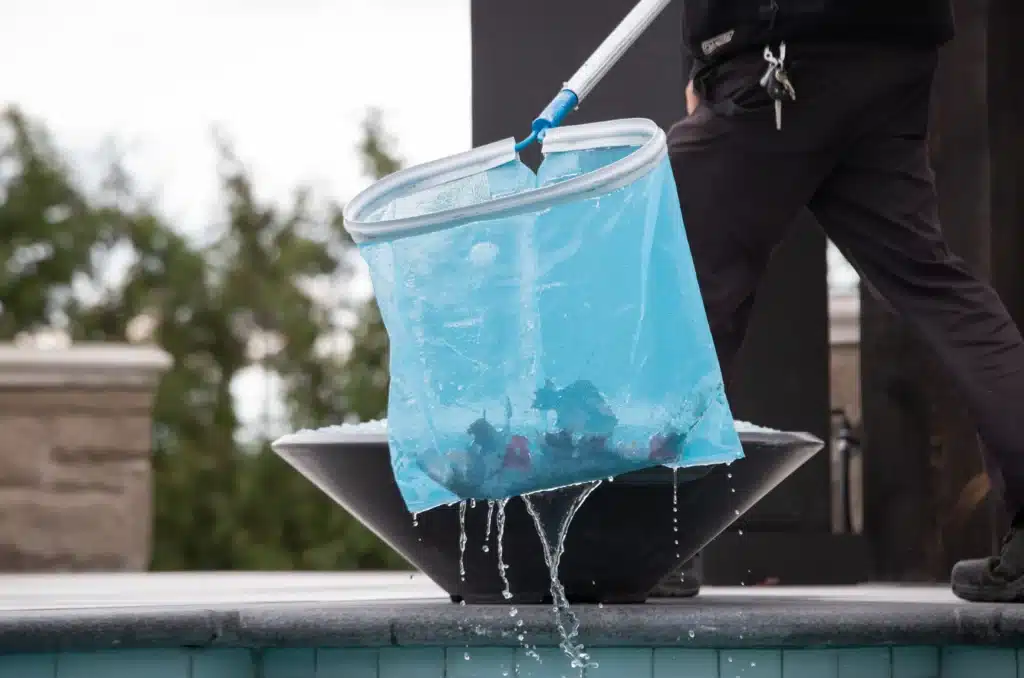 Person skimming debris from pool surface during pool opening