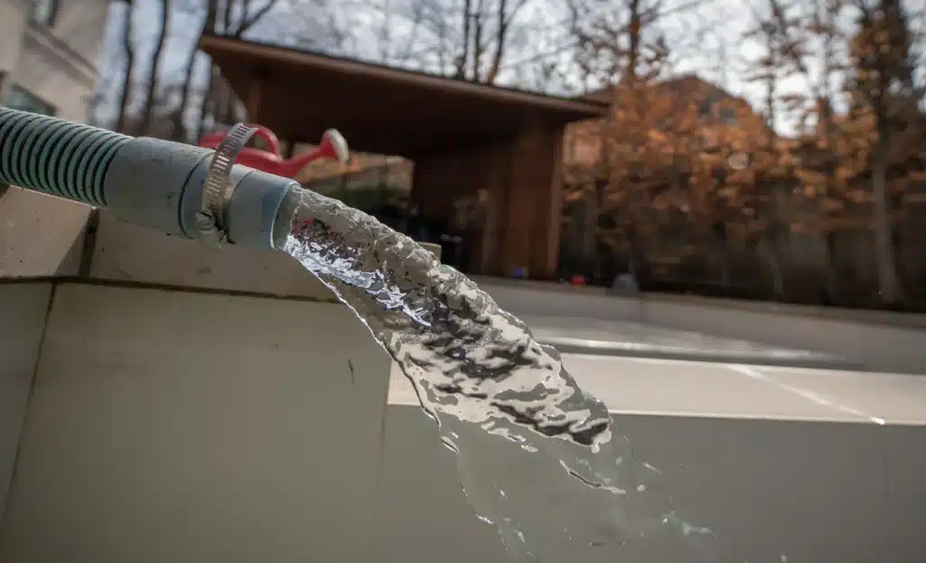 Water flowing from a hose into a swimming pool during spring pool opening and refilling process in a residential backyard.