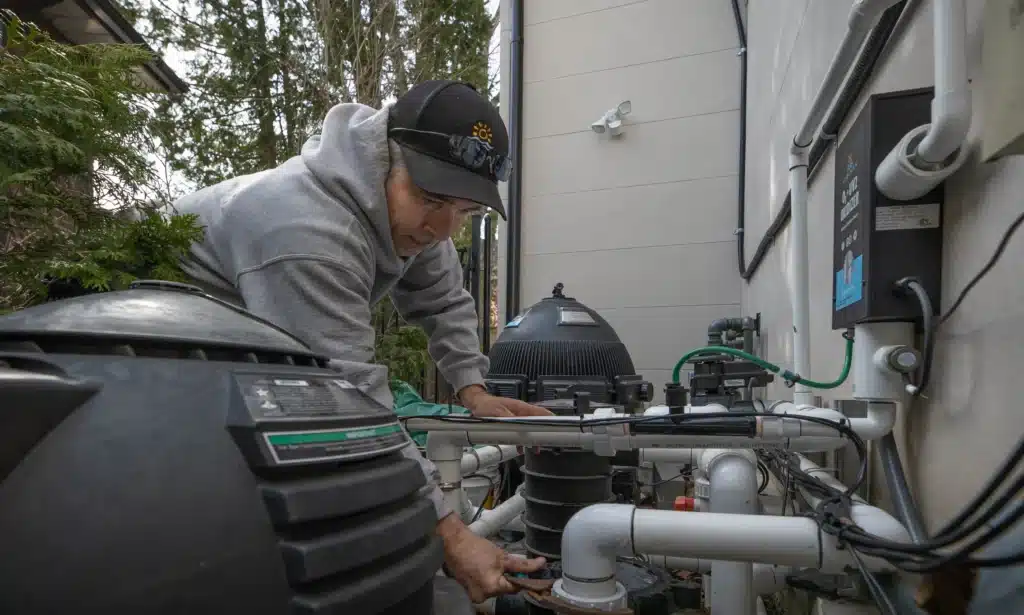 Pool technician inspecting and reconnecting pool filtration and pump equipment during spring pool opening service.