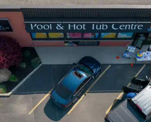 Aerial view of the Gib-San Pool & Hot Tub Centre storefront with cars in the parking lot and people gathered near a display table outside.