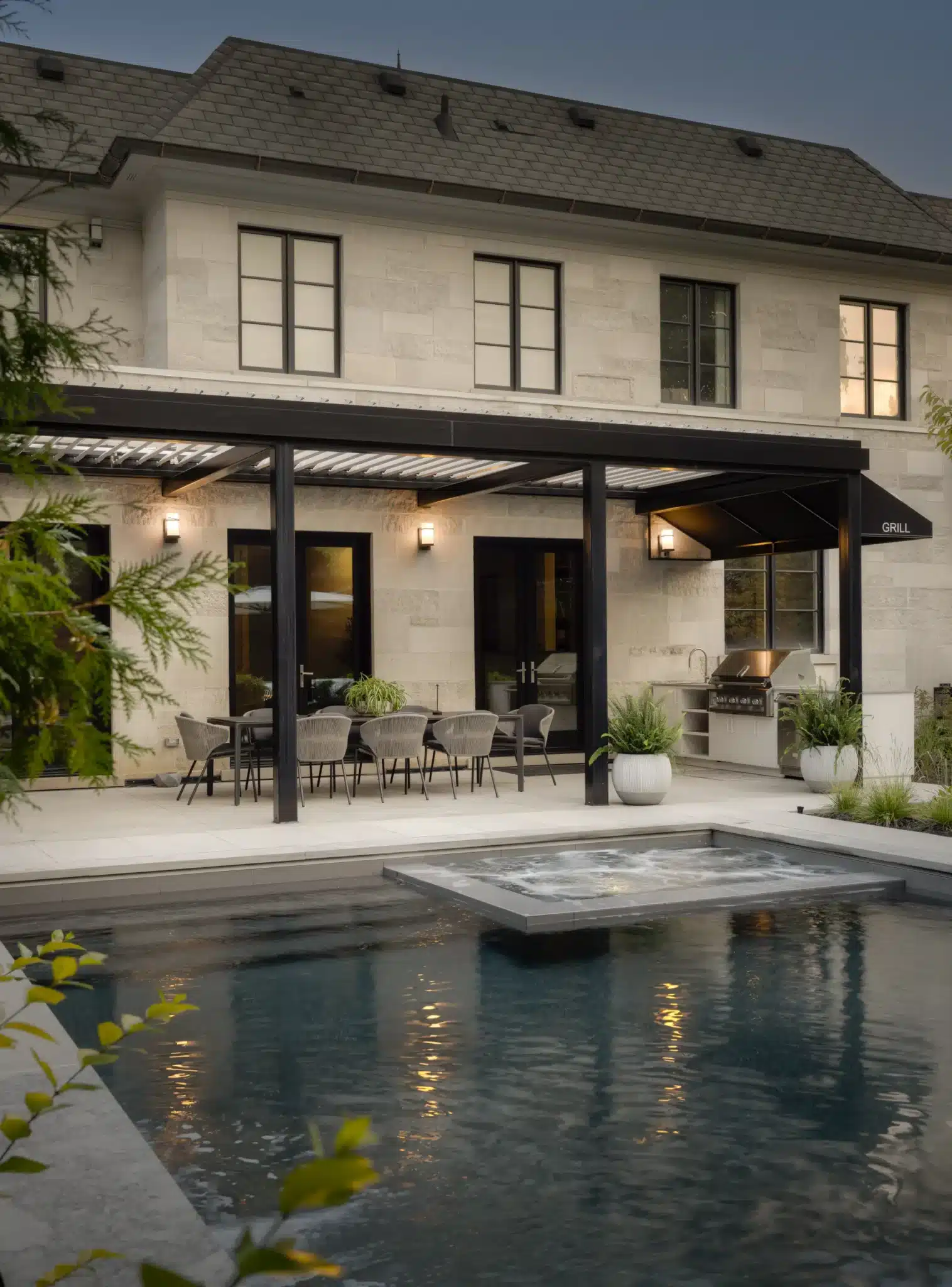 Luxury backyard pool and raised spa beside a covered patio with outdoor dining, built-in grill, and modern stone home exterior.